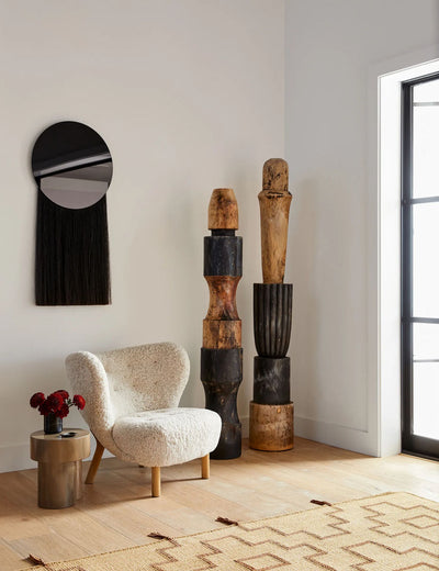Decorative boho room with a textured armchair, wooden sculptures, and a mirror.
