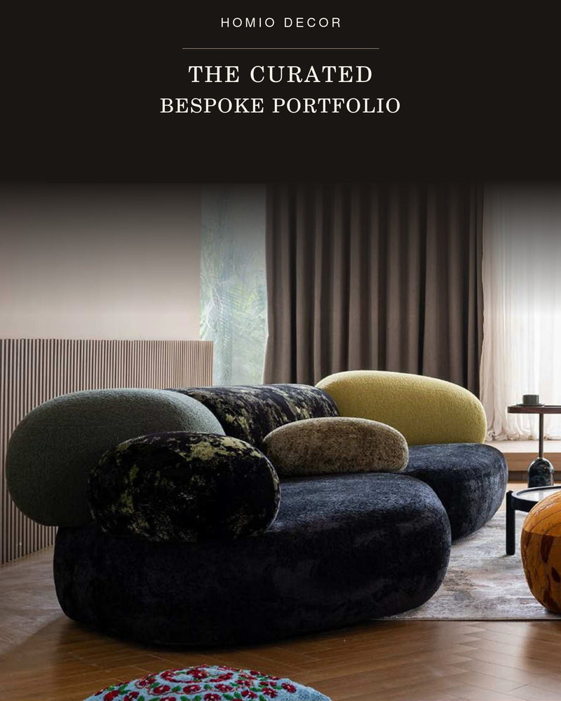 A modern curved lounge sofa with oversized rounded cushions in dark charcoal, olive green, mustard yellow, and textured beige, shown in a styled interior setting. 