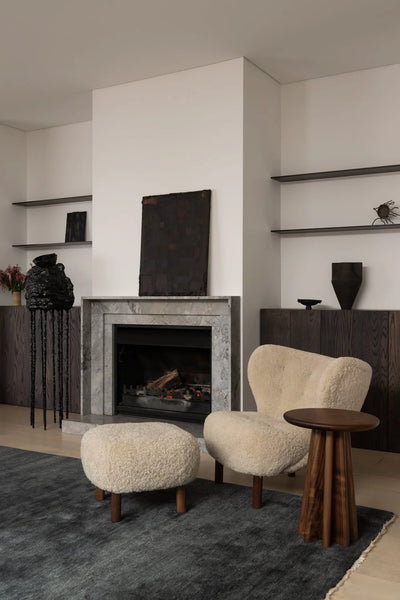 Modern living room with a fireplace, armchair, ottoman, and side table.