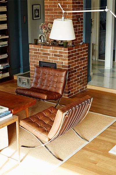 Modern living room with brown leather chairs, a brick fireplace, and a wooden floor.