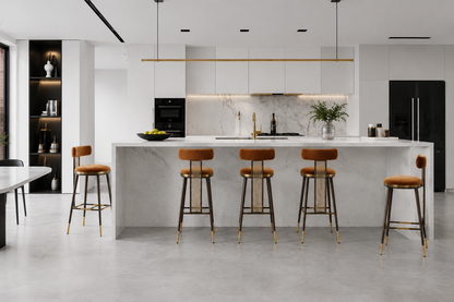 A modern kitchen island with a white marble countertop and backsplash, surrounded by four bar stools with brown leather seats and gold-toned metal legs. The kitchen features white floating cabinets, a black refrigerator, and a concrete floor.