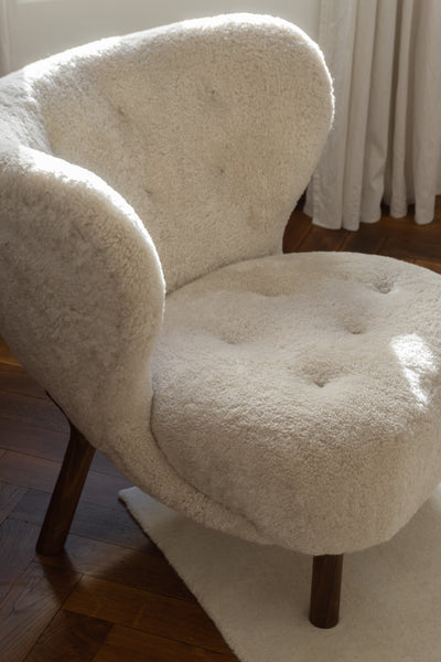 White fluffy armchair on a wooden floor with a white rug