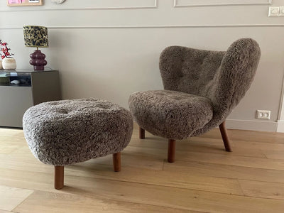 Brown textured chair and ottoman on a wooden floor with a lamp and cabinet in the background.